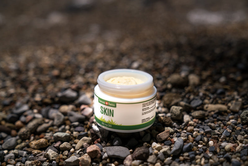 Tarro abierto de bálsamo CBD Skin de Formula Swiss, 300 mg de CBD, en una playa de guijarros